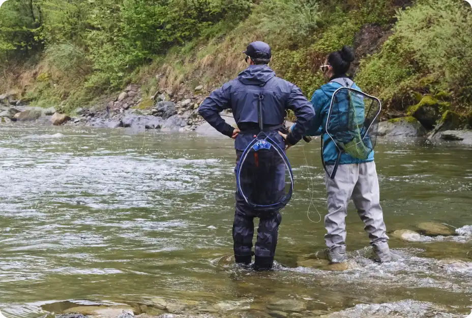 Two anglers wading and reading an alpine river during a beginner friendly fly fishing lesson