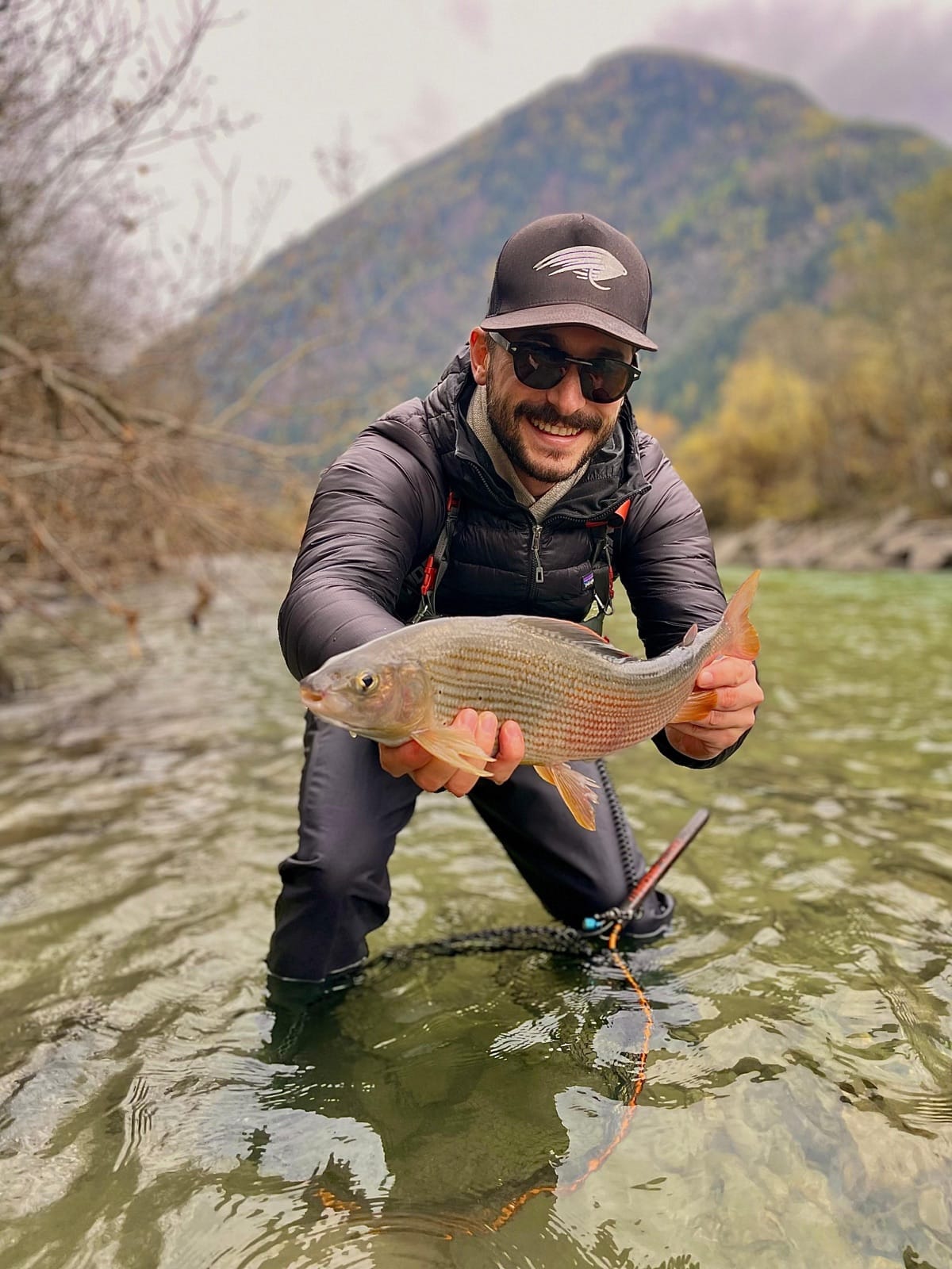 Giulio Pattaro inginocchiato in un fiume alpino con un temolo selvatico in mano