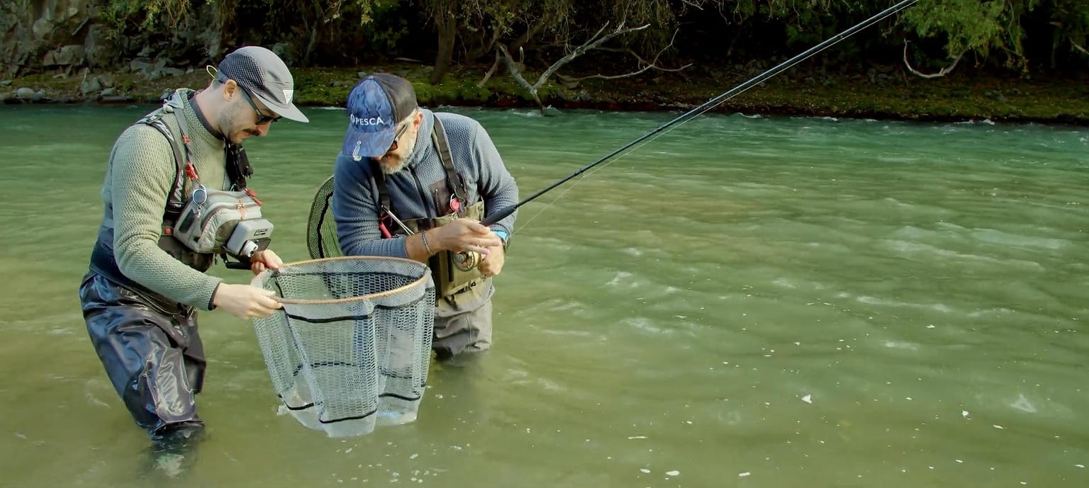 Due pescatori guadinano una trota in un fiume alpino delle Dolomiti