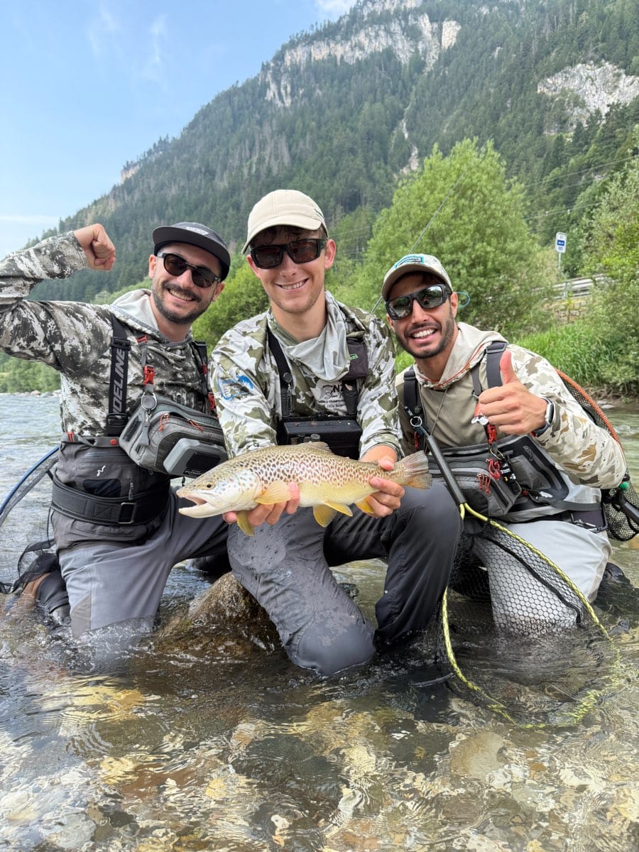 Tre pescatori a mosca in un fiume mostrano una trota fario selvatica catturata durante una giornata intera di guida