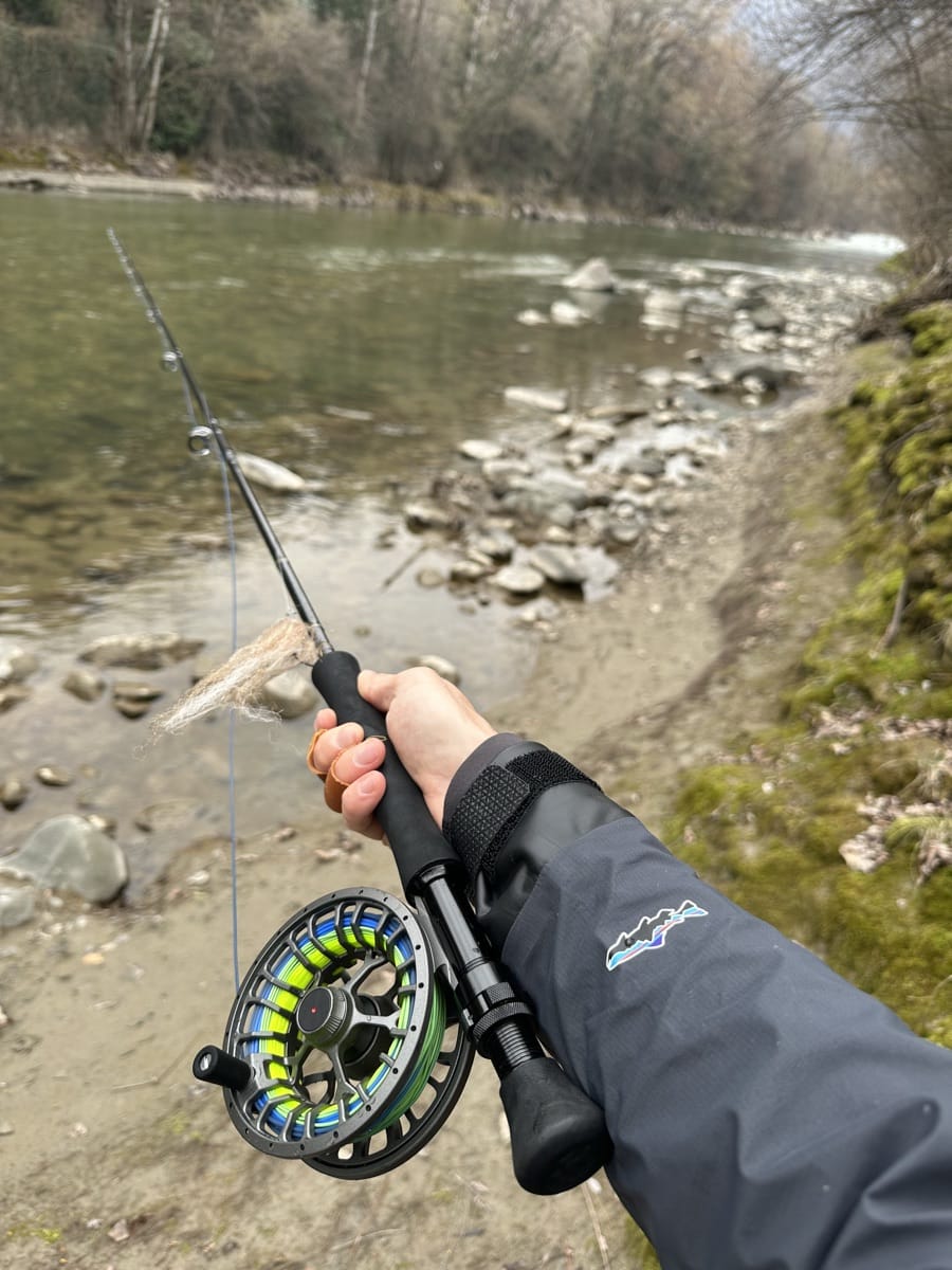 Pescatore con canna e mulinello rivolti verso un fiume di montagna